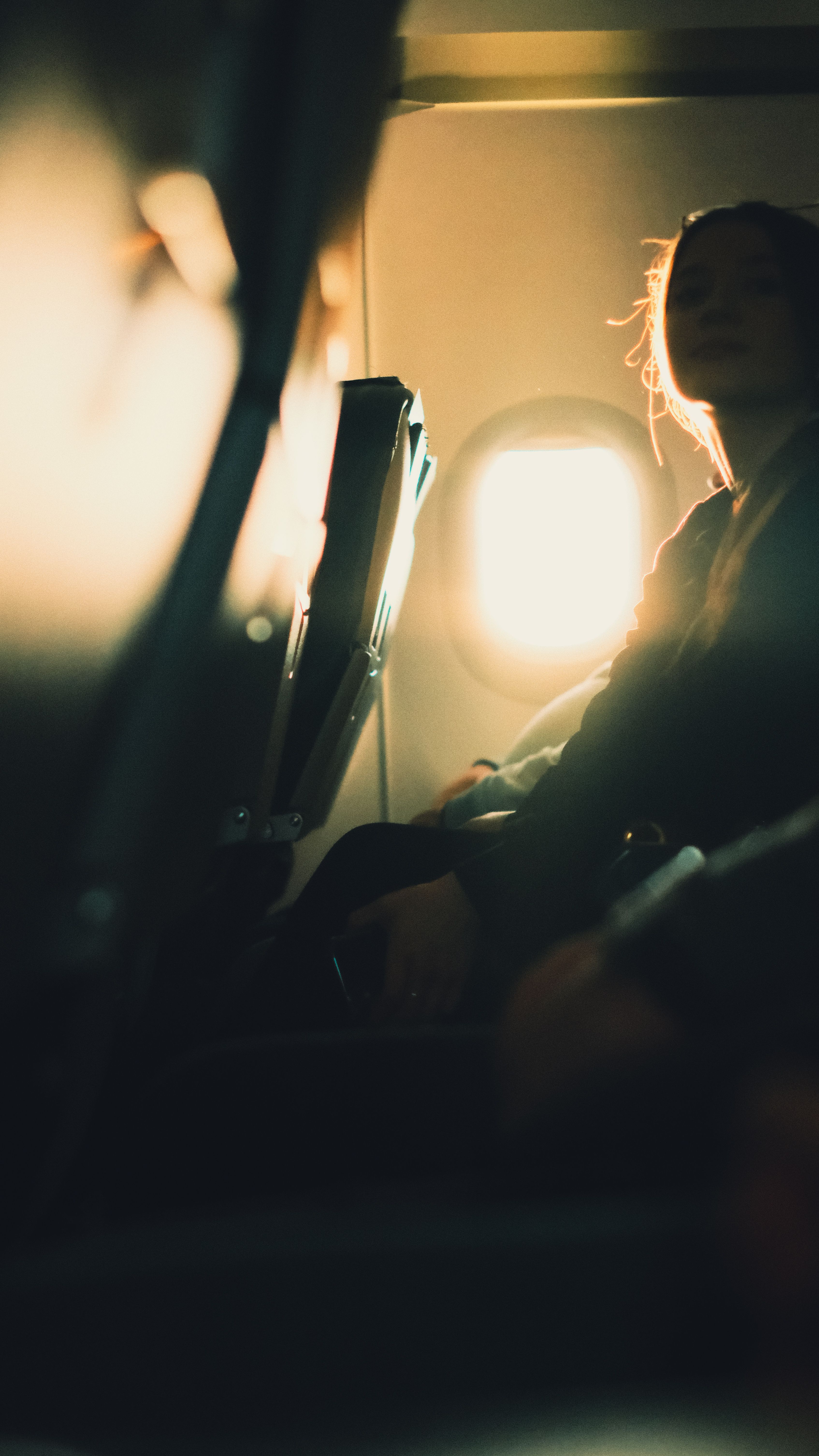 A woman silhouetted by sunlight while sitting inside an airplane, creating a serene atmosphere.