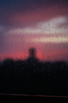 Captivating raindrops on a window against a twilight sky with blurry silhouette.