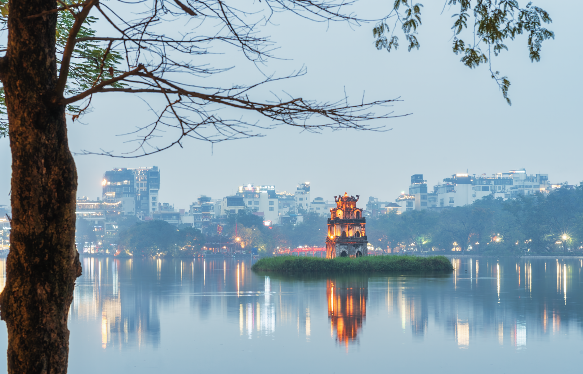 Serene view of the illuminated Turtle Tower on Hoan Kiem Lake in Hanoi during the evening, surrounded by city lights.