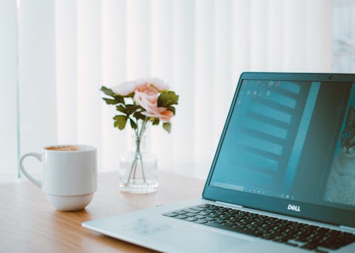 Black and Gray Dell Laptop Beside White Ceramic Mug Flower