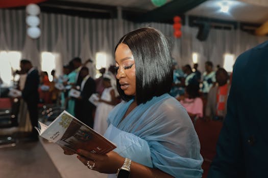 A stylish woman in a blue dress reads a program at a ceremonious indoor gathering.