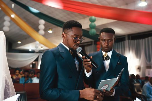 Two men in suits speaking at an indoor ceremony with elegant decor.