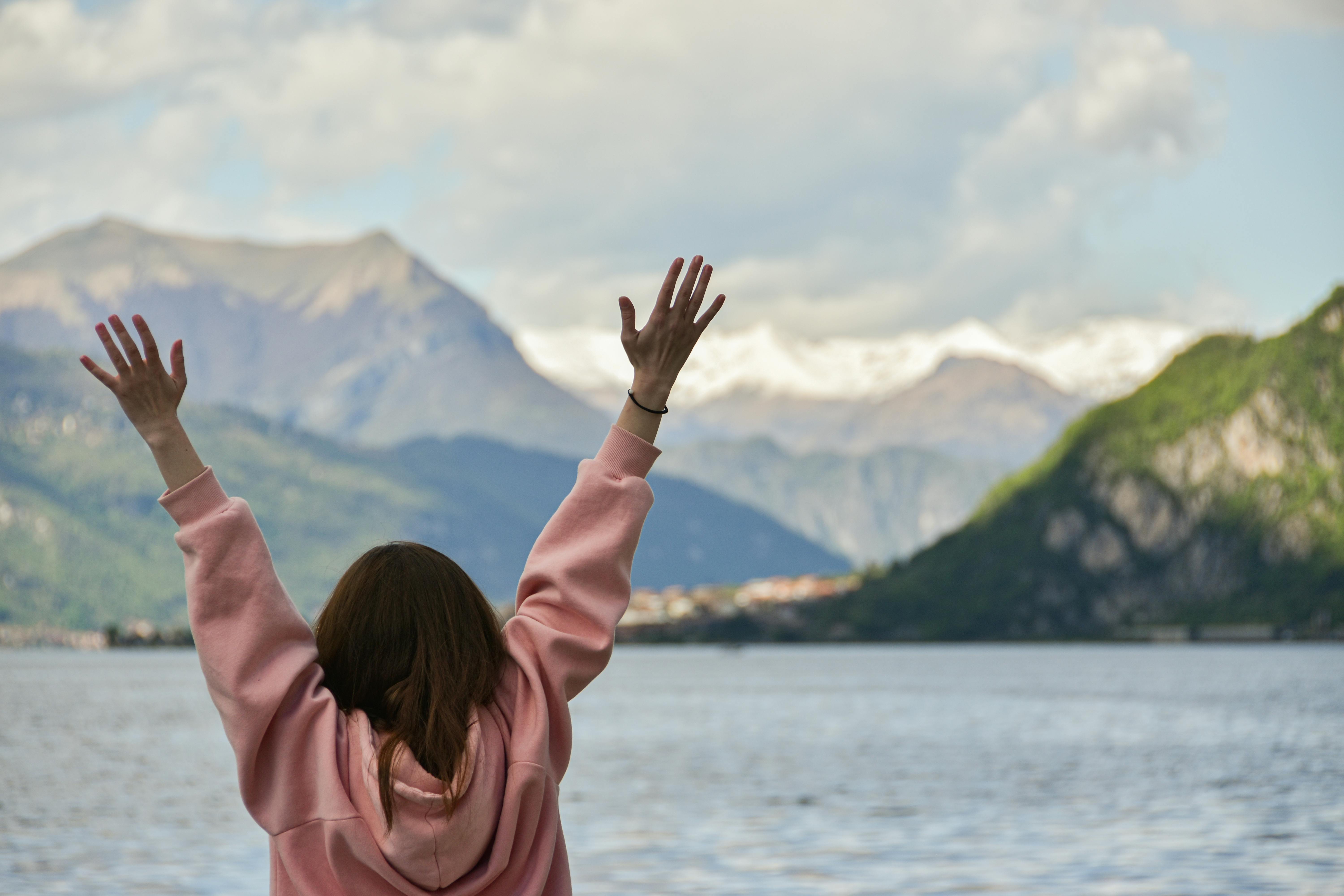 A woman with raised hands enjoying the scenic view of mountains and lake.