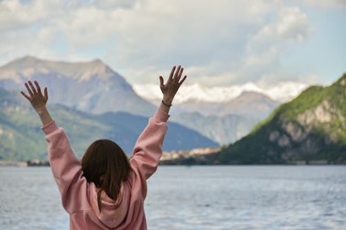 Woman with Hands Raised Standing near Water in Mountains Landscape
