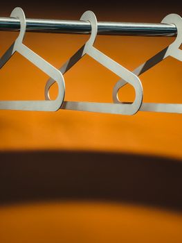 Three wooden hangers hanging on a rod against a vibrant orange background.