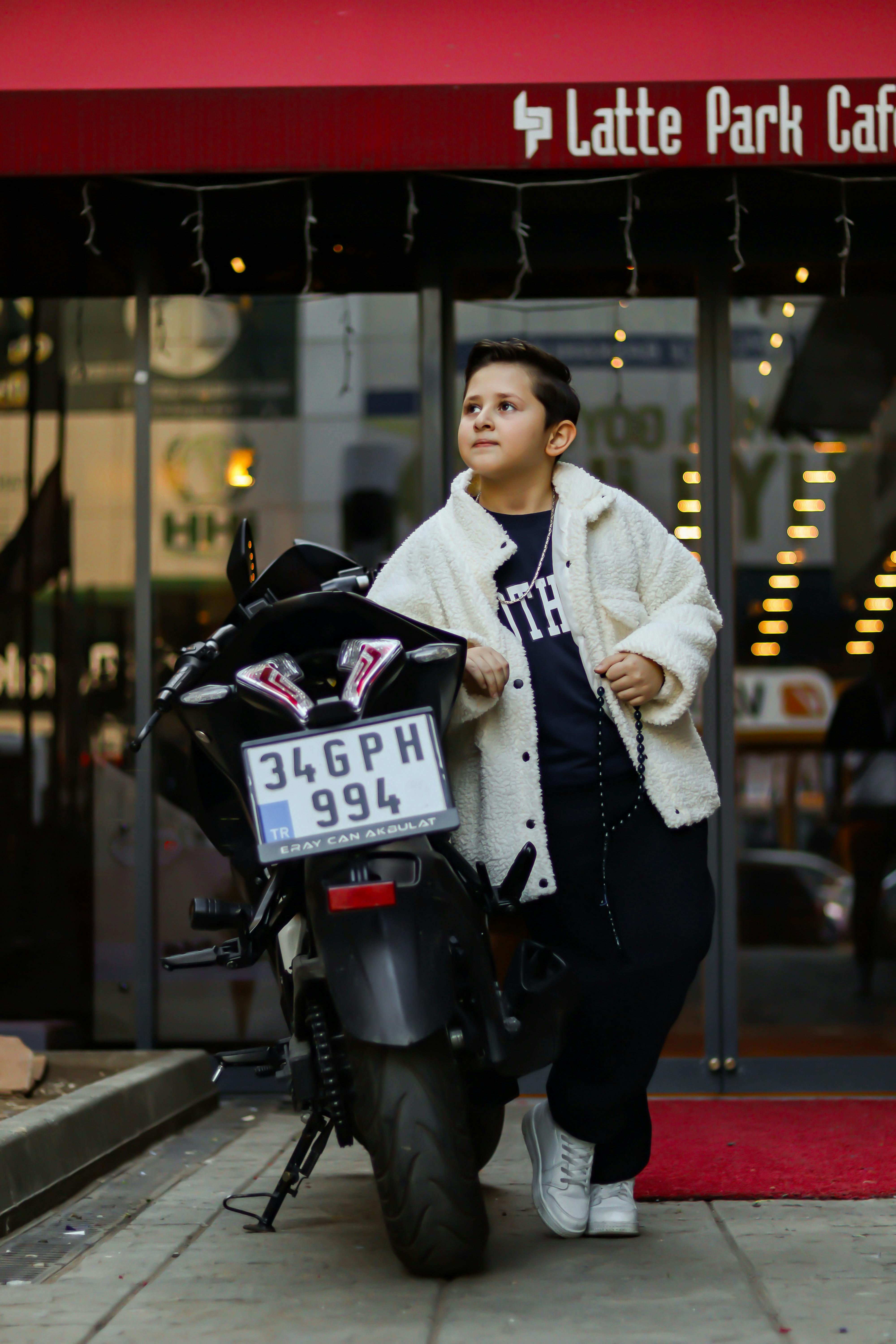 Child posing stylishly with motorbike in city street, showcasing modern fashion.