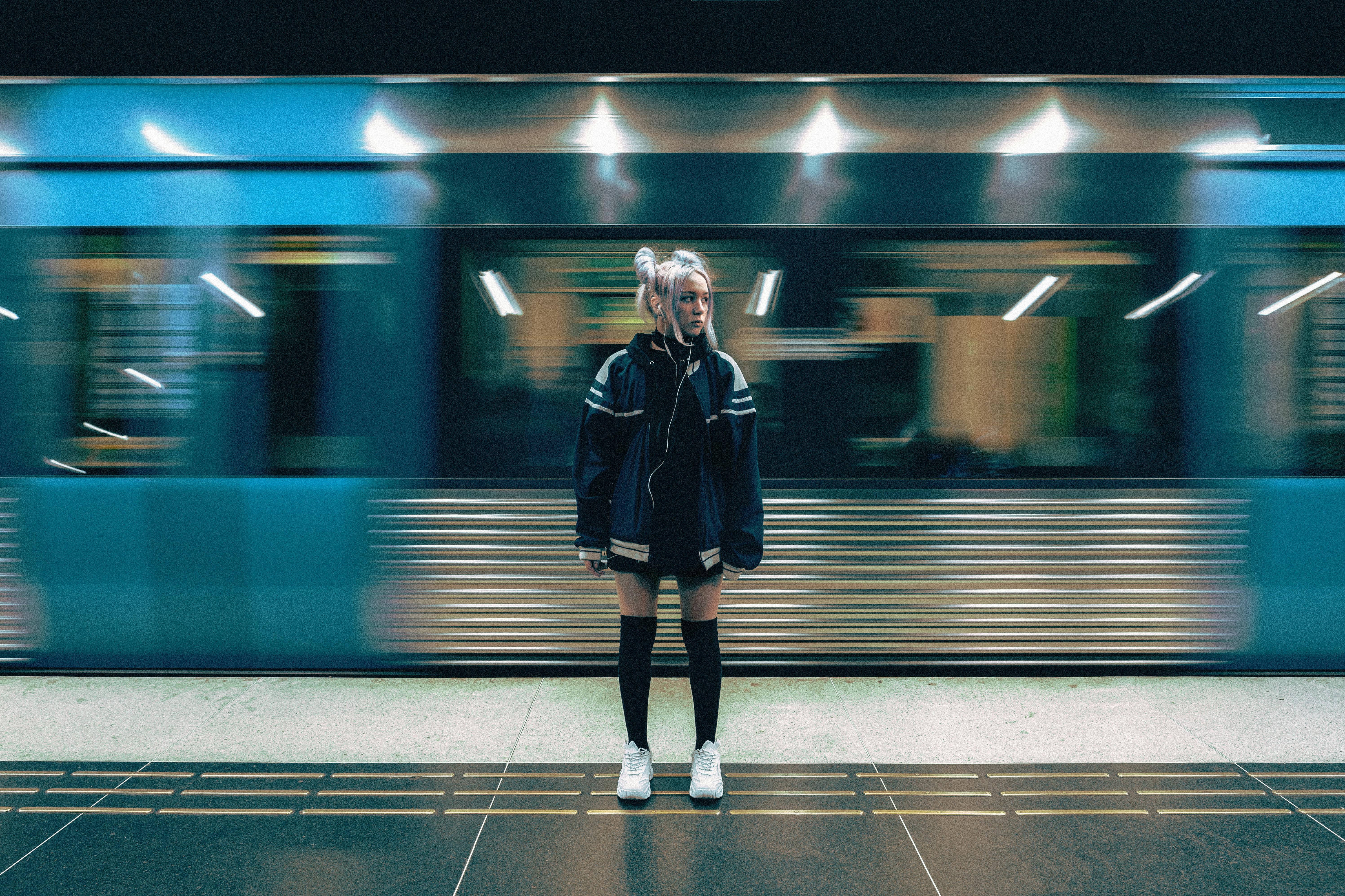 young woman in a mini and oversized jacket with gray hair tied in ponytails with a departing subway in the background