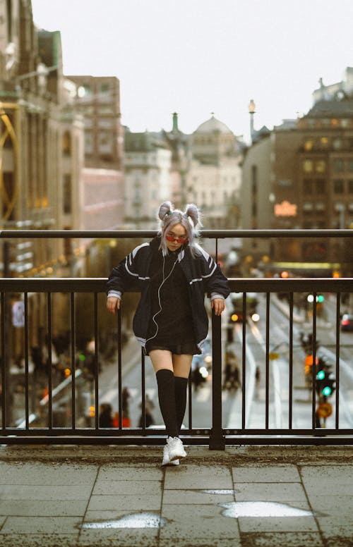 Young Woman in a Mini and Oversized Jacket with Gray Hair Tied in Ponytails Leaning on the Overpass Railing