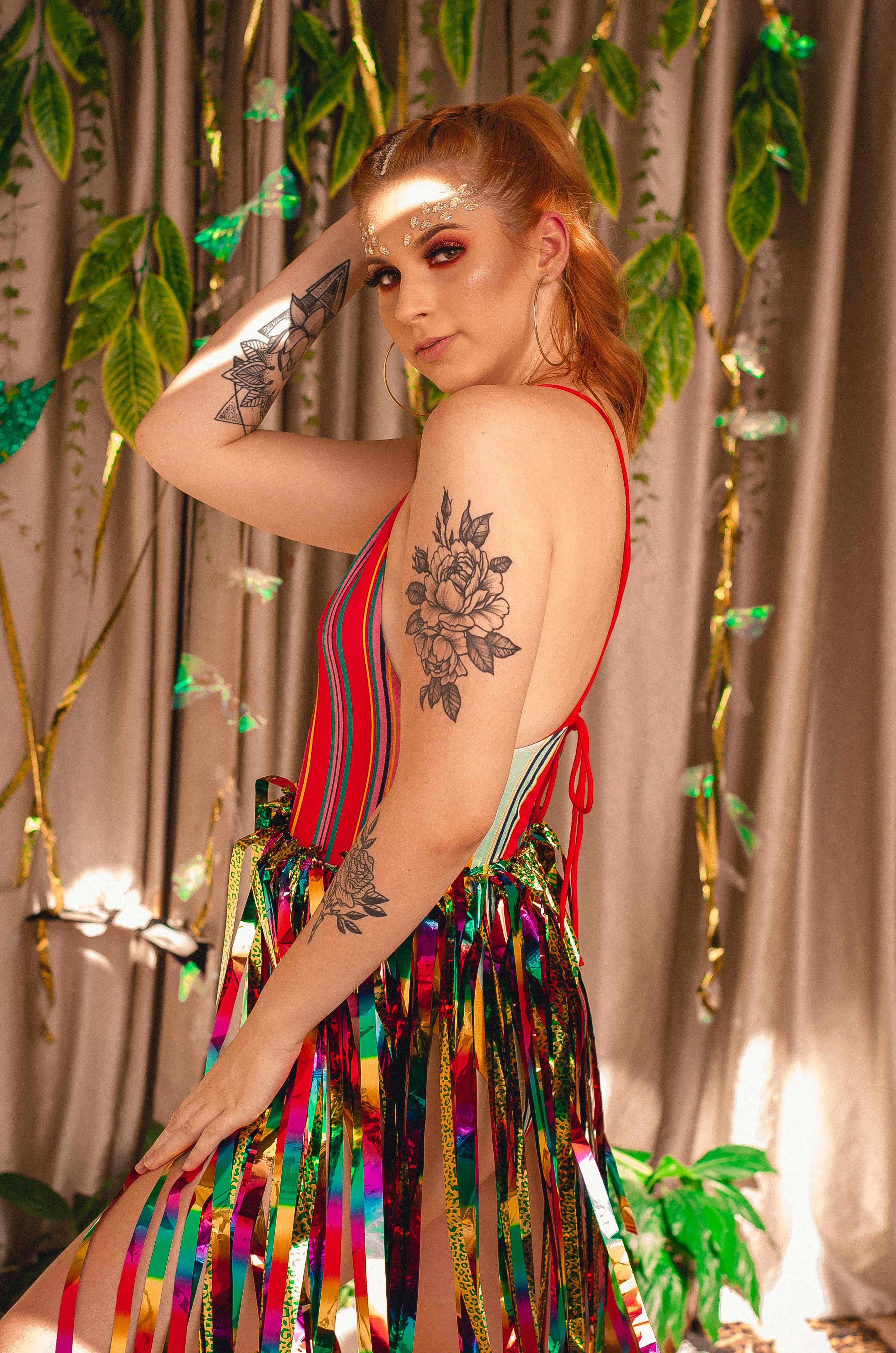 一位纹身精美的女人身着充满活力的彩虹服装，背景是绿叶