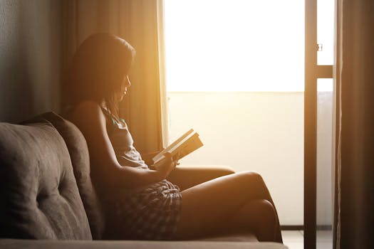 Woman reading a book on sofa by window with morning sunlight. Calm and relaxing atmosphere.