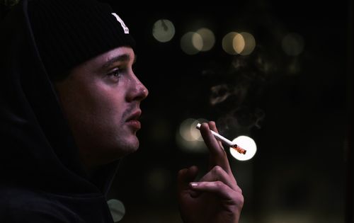 Free Portrait of a man wearing a beanie, smoking outdoors at night against a blurred background. Stock Photo