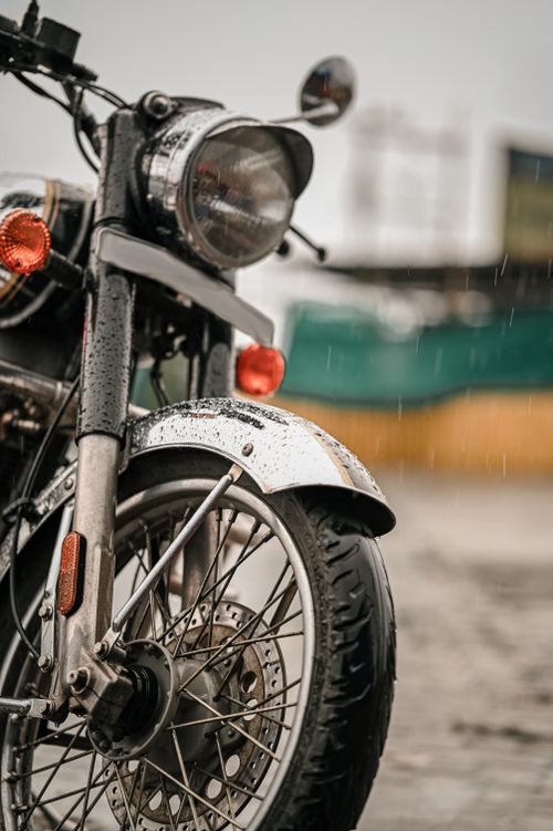 Free A detailed view of a motorcycle parked on wet pavement amidst rainfall in an urban environment. Stock Photo