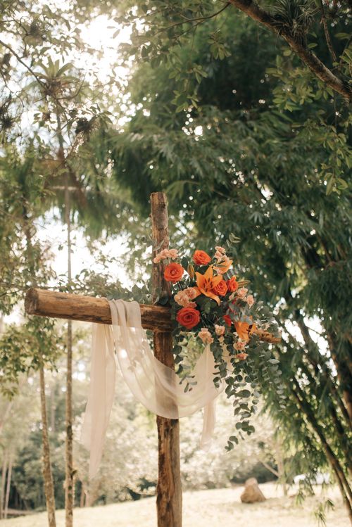 Free A rustic wooden cross adorned with vibrant flowers in a tranquil forest setting under soft sunlight. Stock Photo