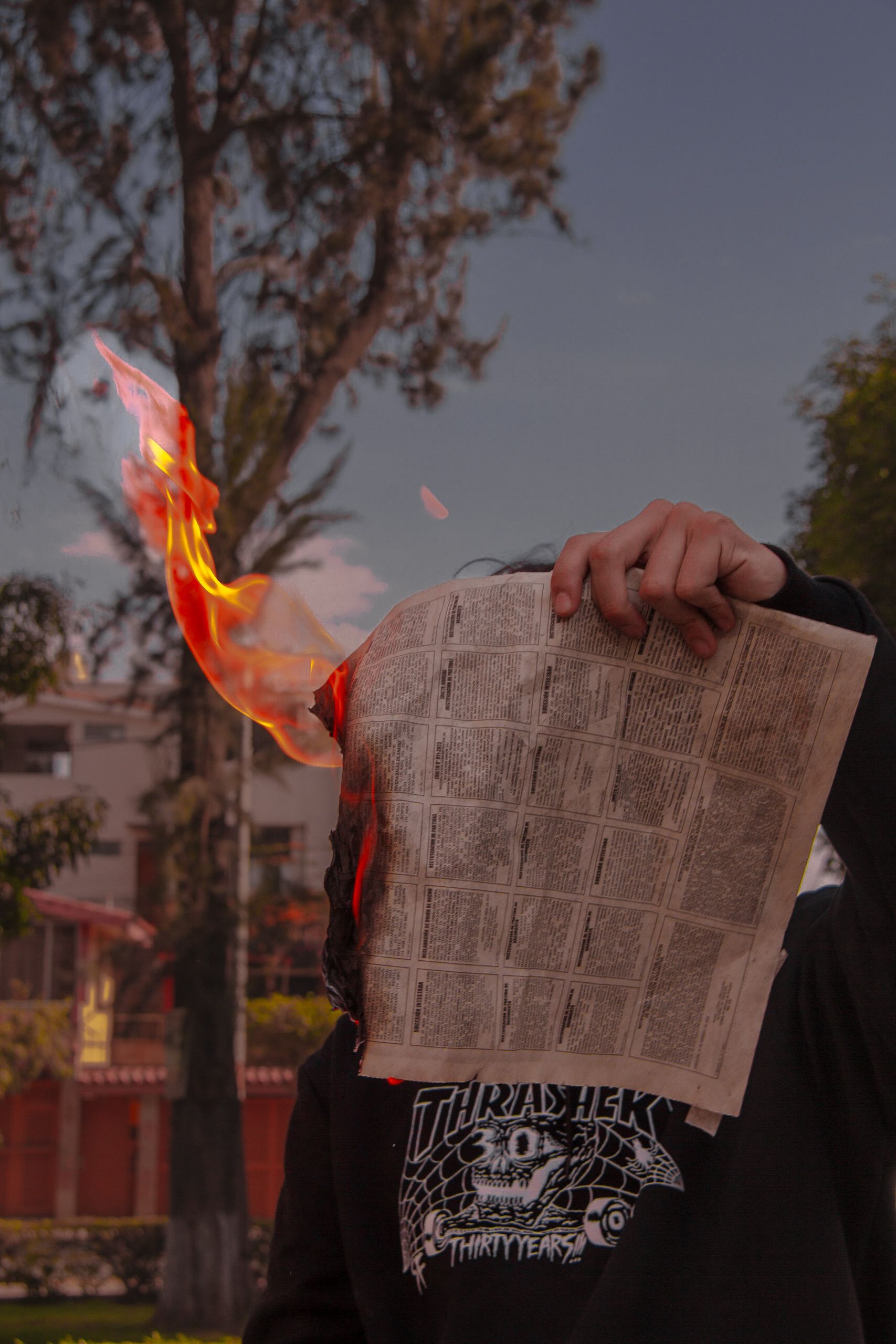 A person holds a flaming newspaper outdoors, capturing a dramatic moment.