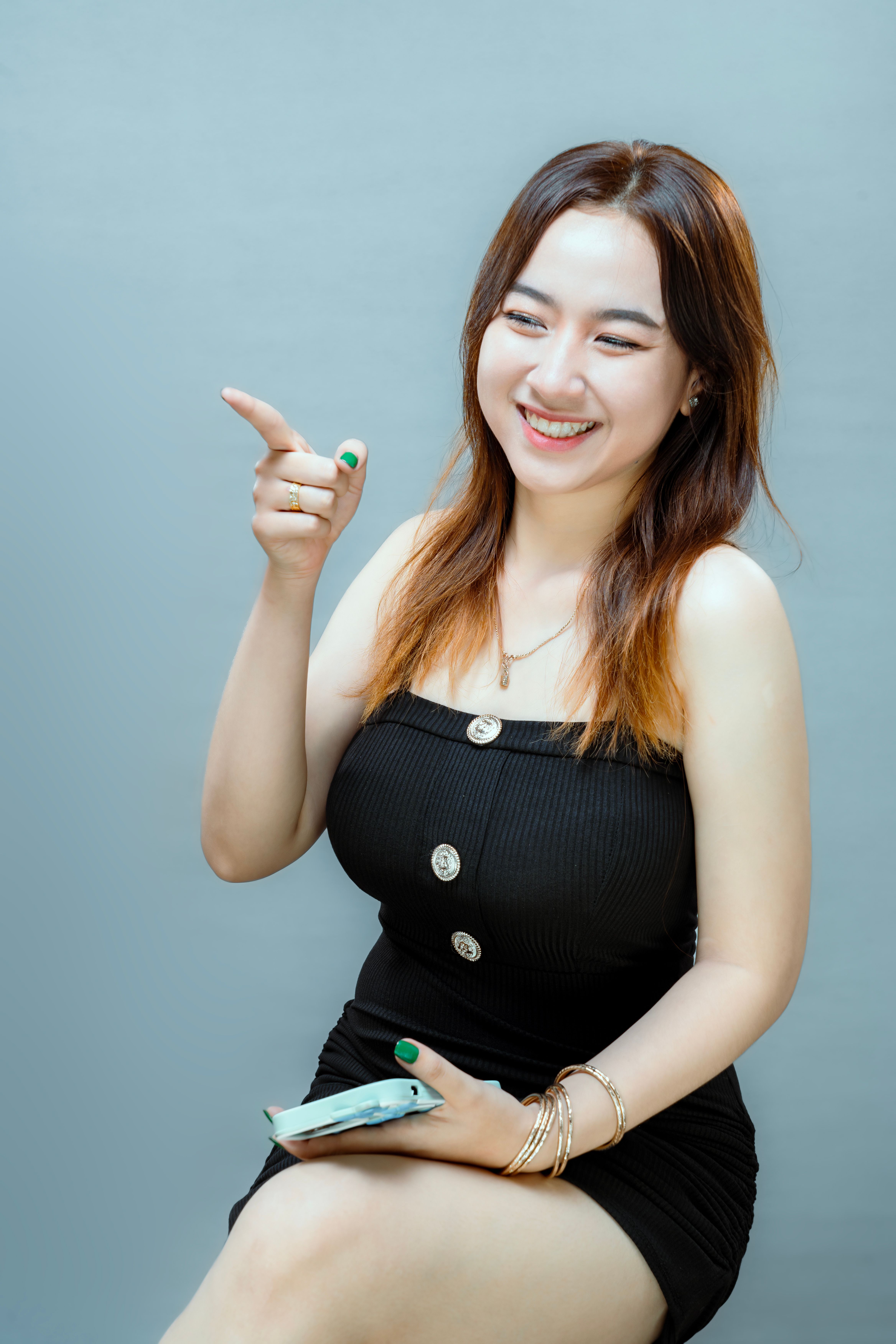 Portrait of a smiling woman in a black dress pointing with joy against a gray background.