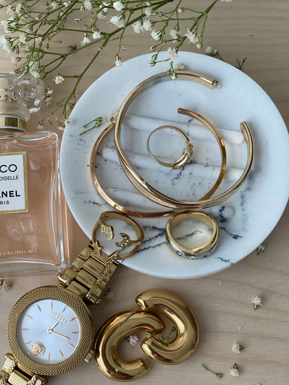 Sophisticated arrangement of gold jewelry and Chanel perfume on a marble plate.