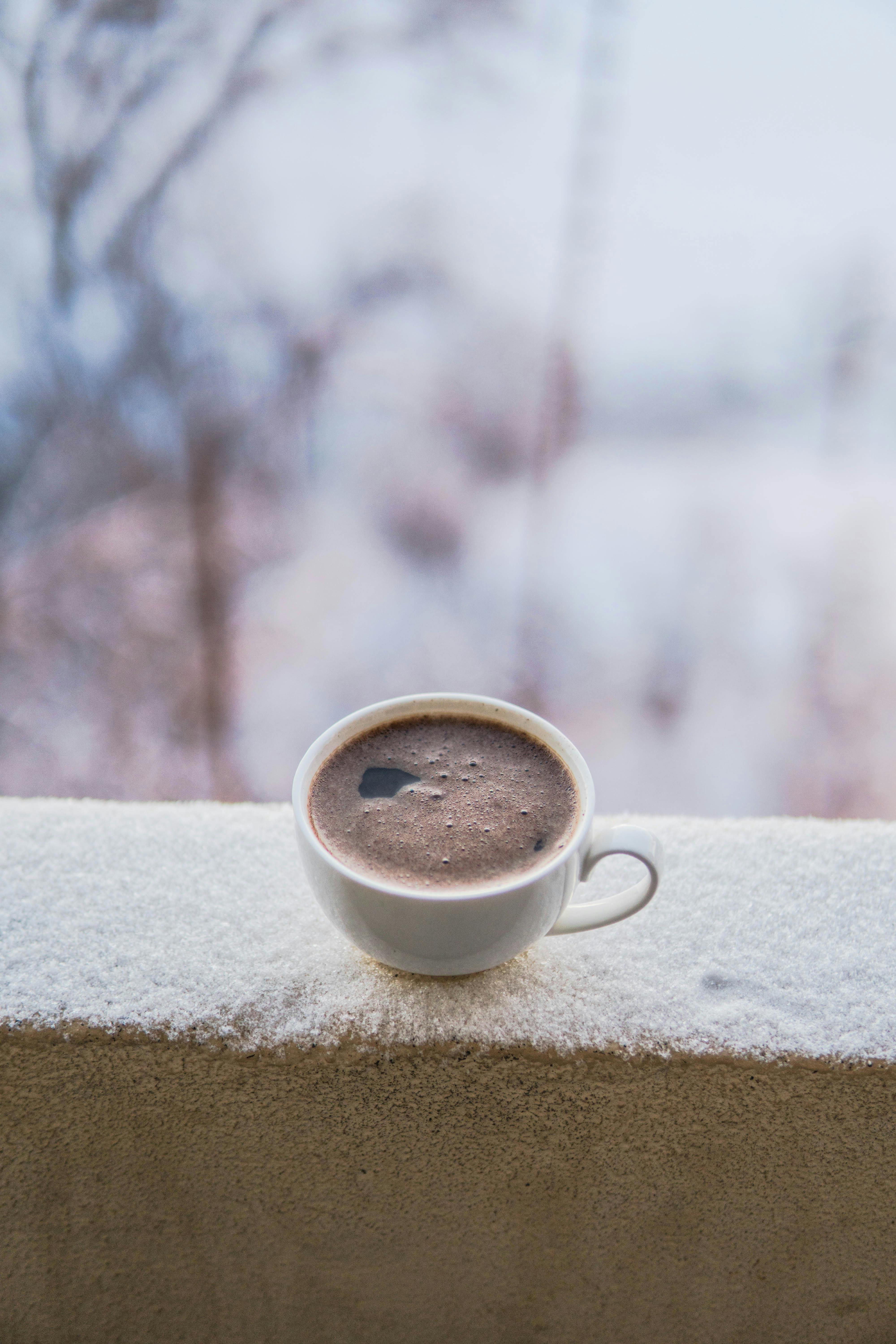 Close-up of a steaming coffee cup on a snowy balcony in Azerbaijan, evoking a cozy winter ambiance.