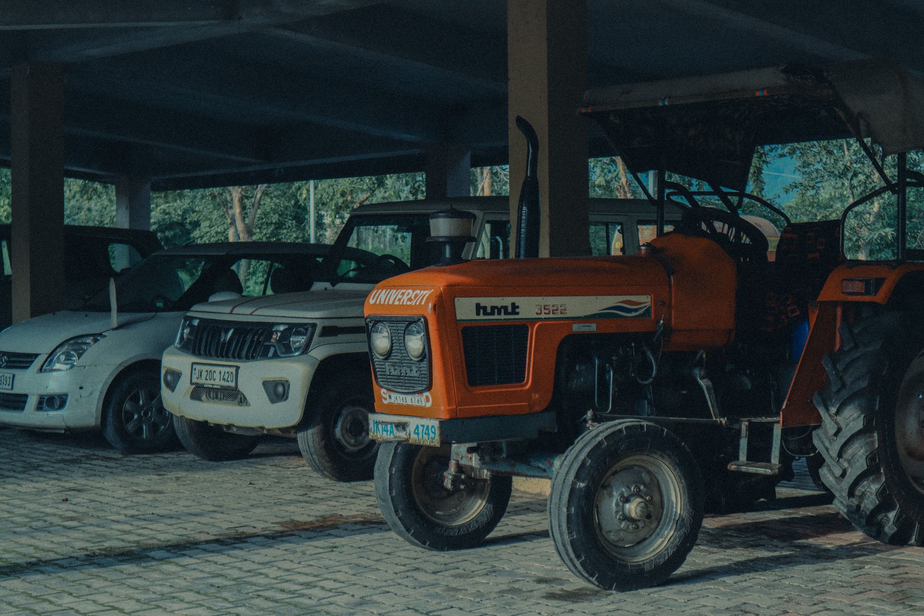 Tractors and cars parked in a covered garage in Jammu, showcasing transportation vehicles.