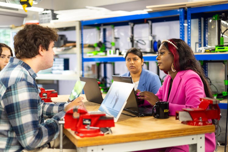 People Sitting At Desk In Workshop And Talking