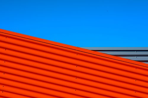 Free Bright red steel wall against a clear blue sky, showcasing minimalistic modern architecture. Stock Photo