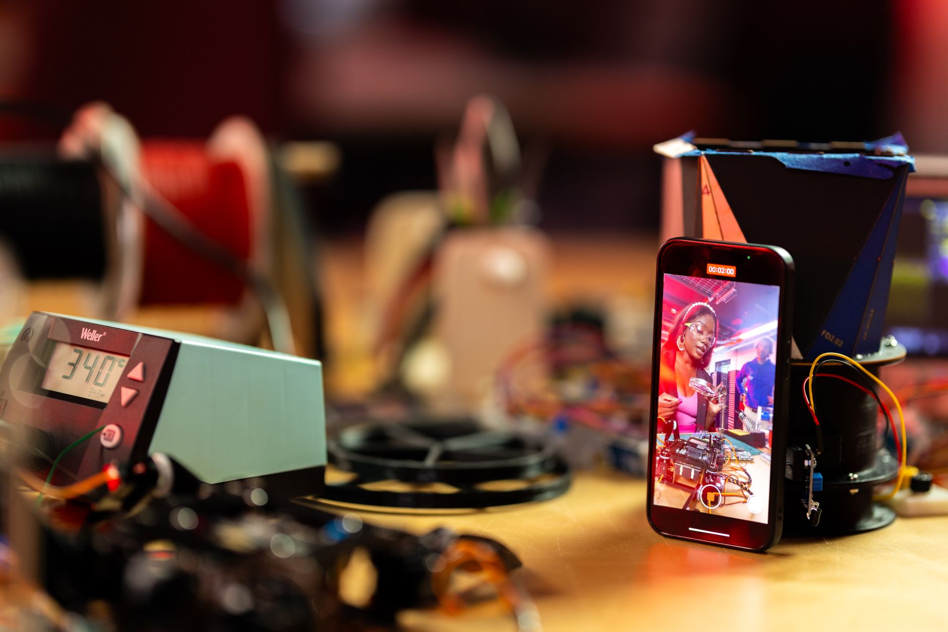 A smartphone capturing a woman at an electronic workshop, surrounded by tech gadgets.