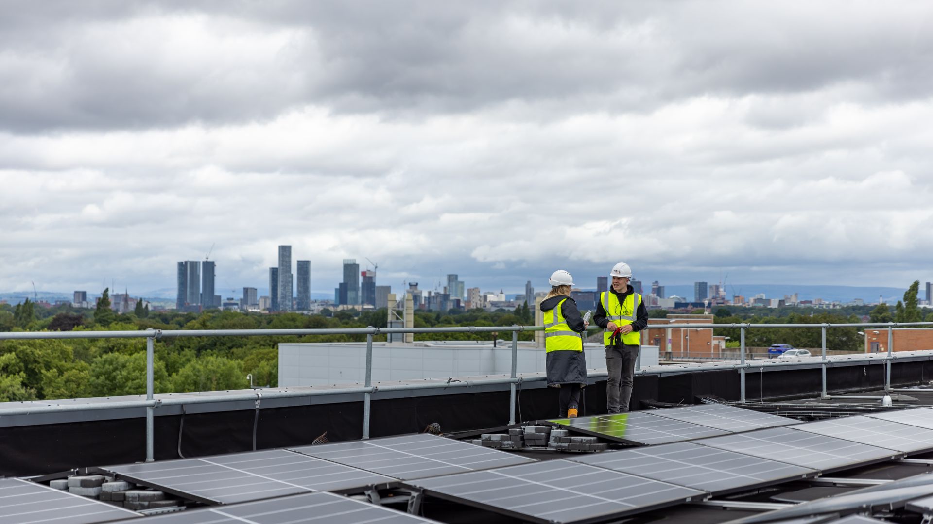 Two workers checking solar panels on a rooftop with a city skyline behind