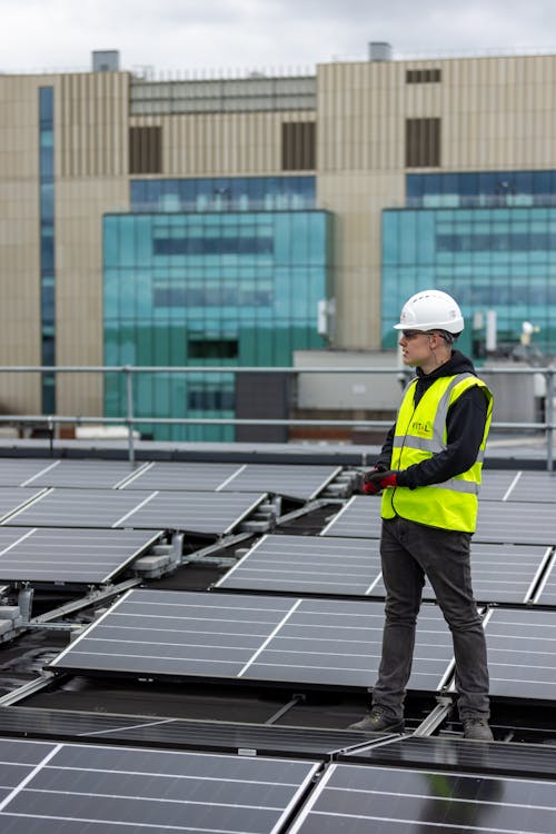 Man in Safety Vest Standing Among Solar Panels on Rooftop