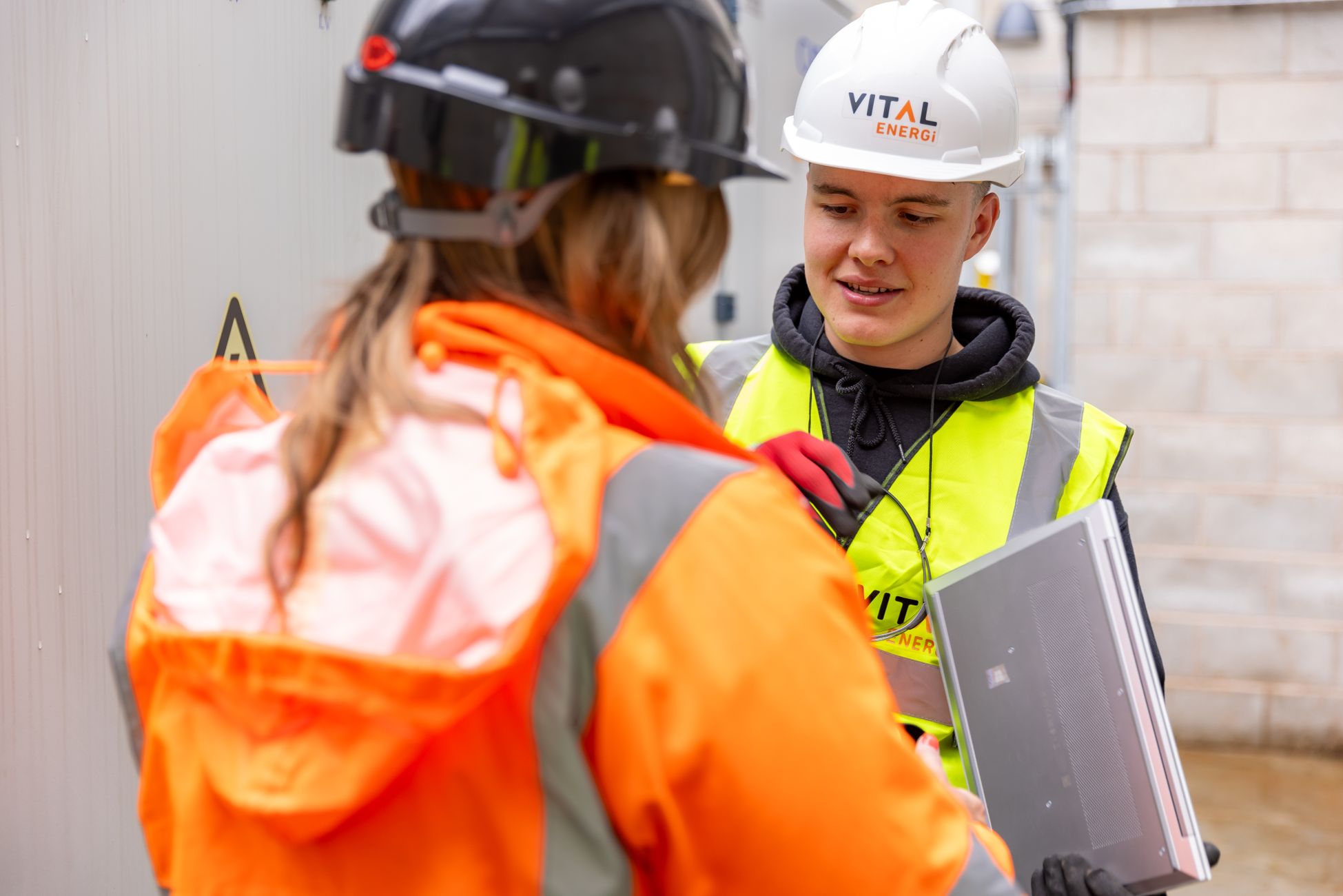 Two construction workers in safety gear collaborate on a project outdoors.