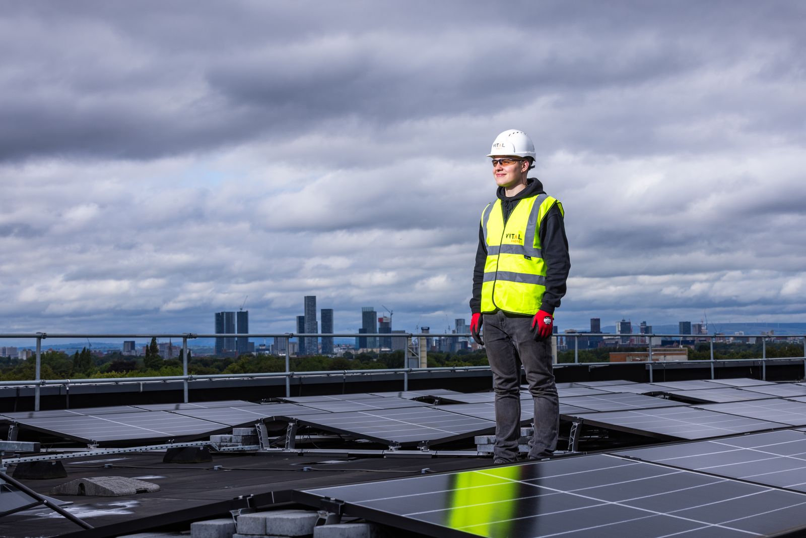 Solar engineer inspecting photovoltaic panels on a large rooftop with an urban skyline in the background