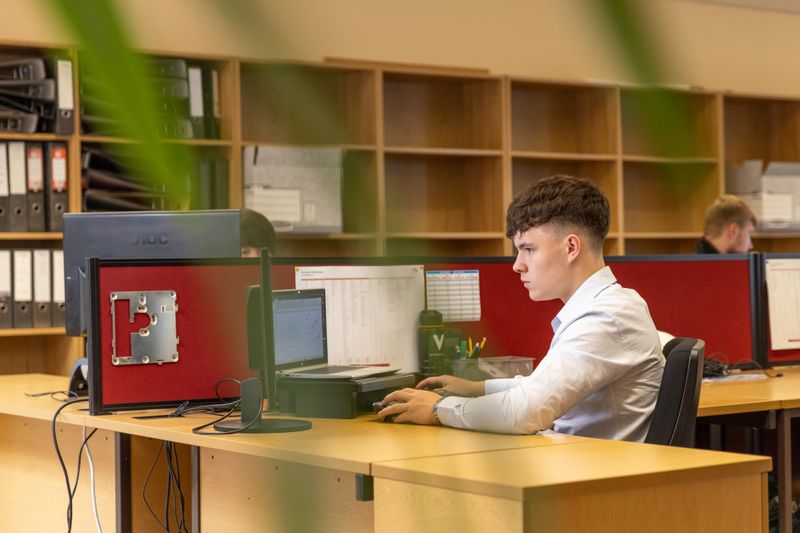 A focused young man typing on a computer in a contemporary office environment.