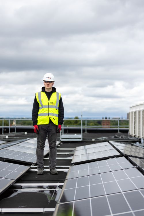 Free Man in safety vest and helmet inspects rooftop solar panels, promoting renewable energy. Stock Photo