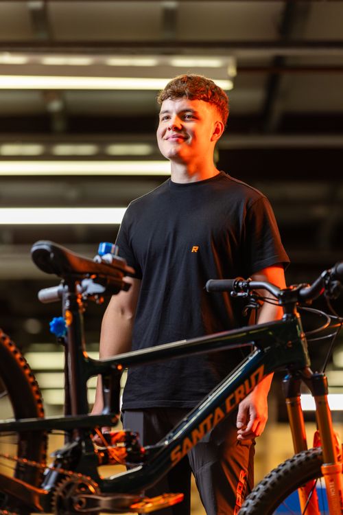 Free Teen smiling while standing beside a Santa Cruz bicycle indoors, showcasing contentment and satisfaction. Stock Photo