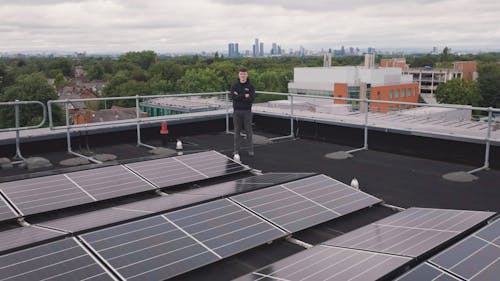 Man Standing by Solar Panels on Rooftop