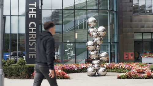 Free A pedestrian walks by a modern reflective sculpture at The Christie building entrance. Stock Photo