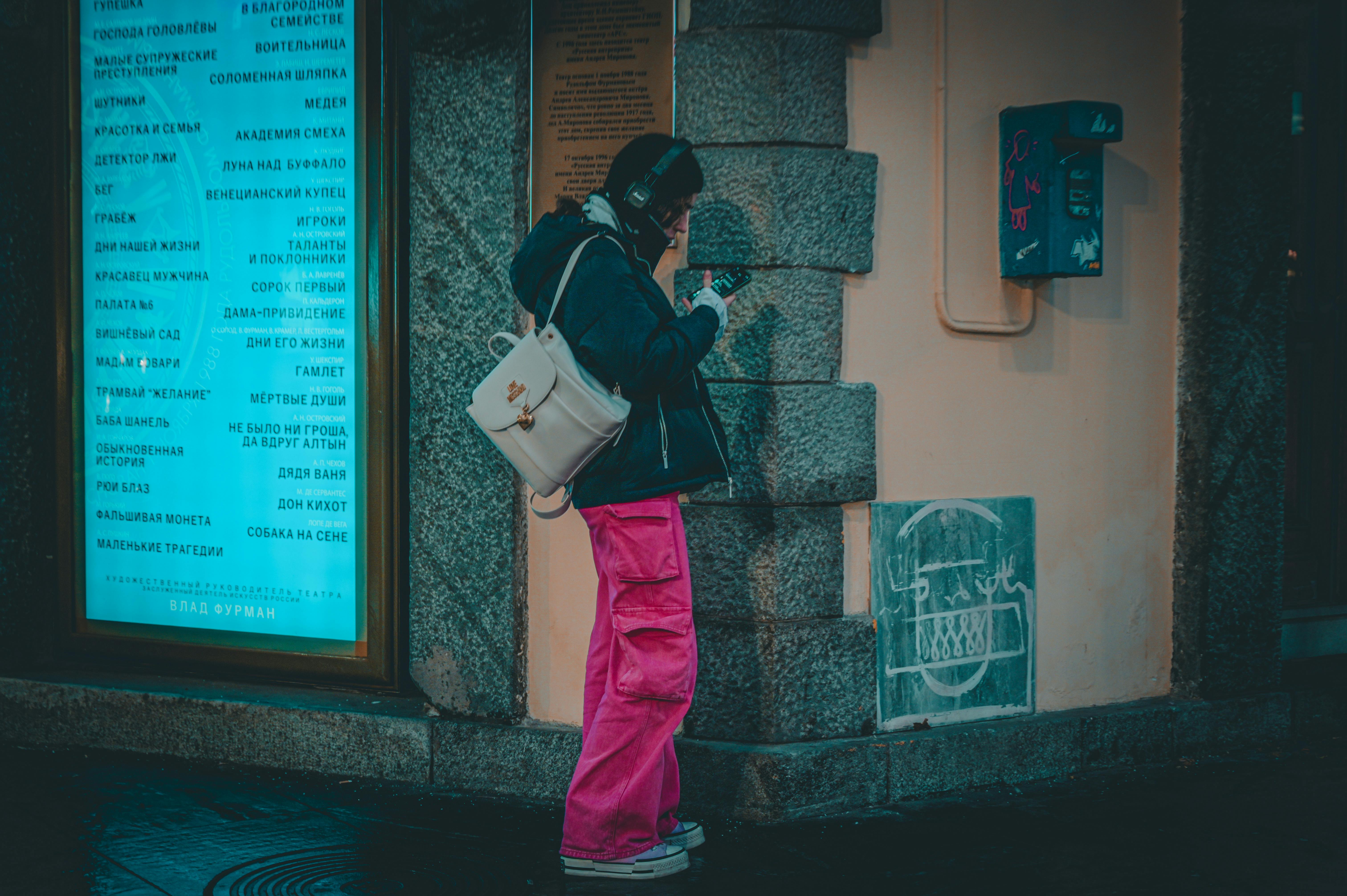A woman with headphones and a backpack checks her phone on a street in San Petersburgo, Russia. - San Petersburgo