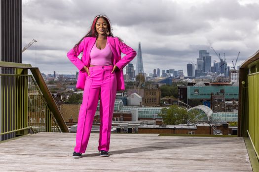 Stylish woman in a vibrant pink suit poses confidently with London's cityscape in the background.
