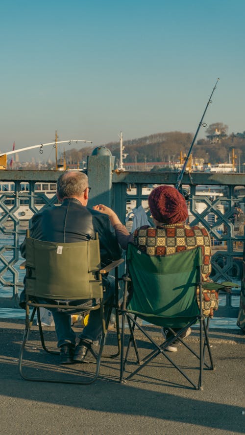 Mature Couple Sitting on a Bridge and Fishing in the Sea 