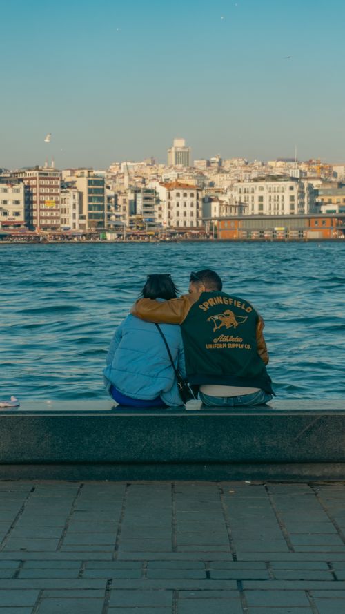 Free A loving couple sits at the riverbank, gazing across Istanbul's Bosporus. Stock Photo