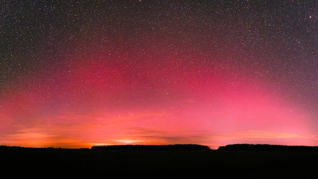 Vivid aurora borealis illuminating the night sky with red hues over a tranquil landscape.