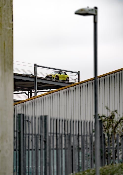 A yellow car is driving on a bridge over a fence