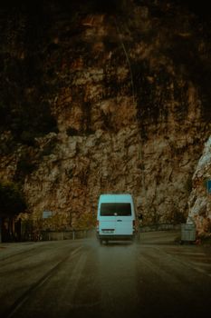 A white mini van travels on a winding road beside a steep rocky cliff, capturing the essence of travel and adventure.