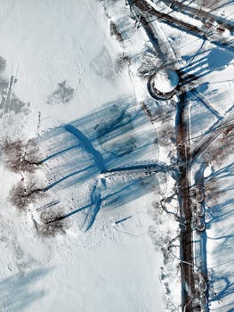 Aerial view of snowy terrain with trees and roads in Minsk, creating dramatic shadows.