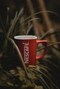 A vibrant red Nescafé coffee mug nestled among lush, tropical plants.