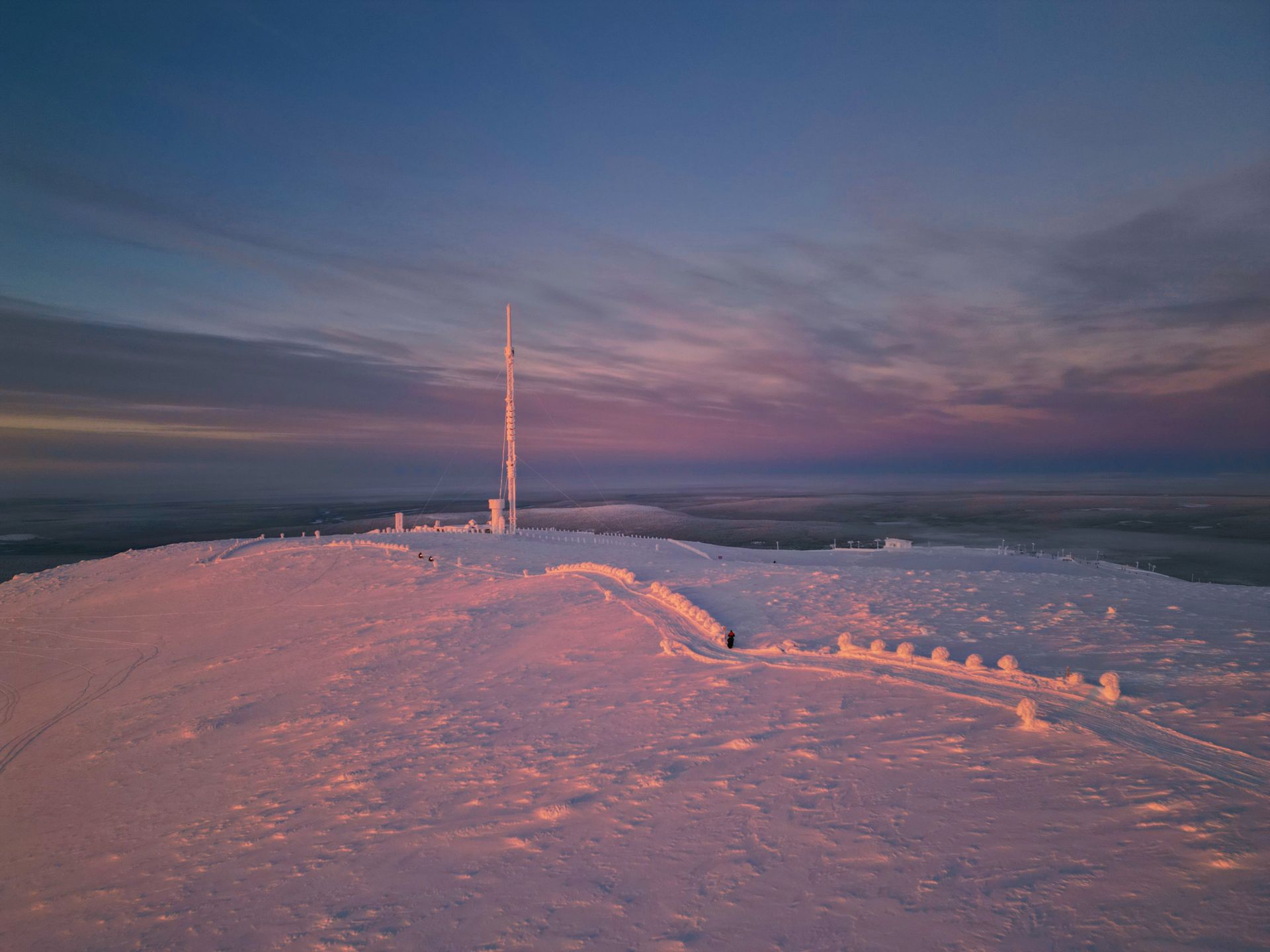 A captivating snowy landscape with a telecommunications tower at sunset in Ylläsjärvi, Finland.
