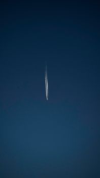 A high-altitude airplane leaves a contrail streaking across a deep blue sky.