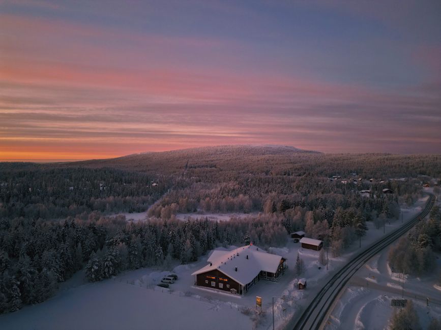 Aerial view of Ylläsjärvi, Finland during a winter sunset with a snow-covered house and road.