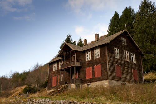 Charming photo of an old Norwegian 'stue' with red shutters, embodying traditional warmth and cultural heritage in its colorful decor and steep roof.