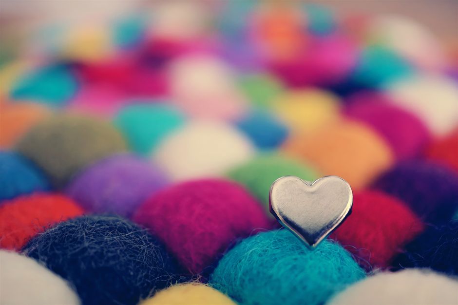 A vibrant display of multicolored wool balls adorned with a heart-shaped pin, showcasing texture and color.