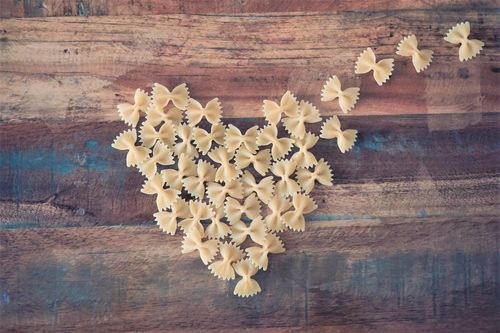 Free Delightful heart-shaped farfalle pasta arrangement on rustic wooden table, showcasing love for Italian cuisine. Stock Photo