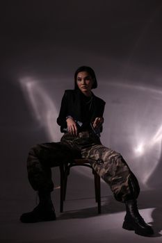 Fashionable woman posing confidently on chair with artistic lighting.